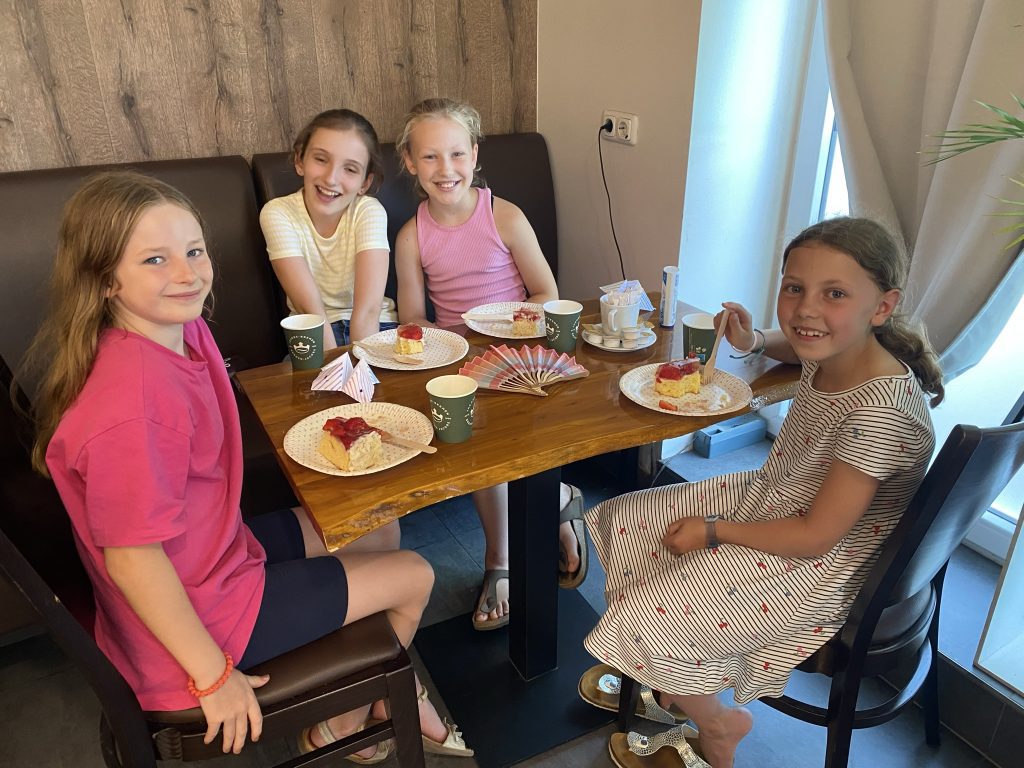 Vier Kinder der Mathematik-Forder-AG sitzen im Café Kling an einem Tisch mit Erdbeerkuchen, Getränken und selbst gebastelten Papierfächern