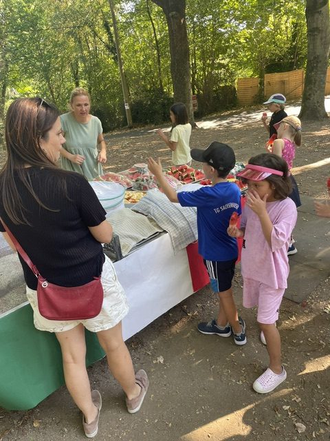 Kinder probieren Wassermelone am Erfrischungsstand des Ferragosto-Fests der Mühlbergschule