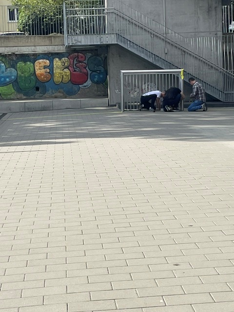Helfer knien am Fußballtor auf dem Schulhof der Mühlbergschule, um das Spielfeld beim Malteser Social Day zu markieren
