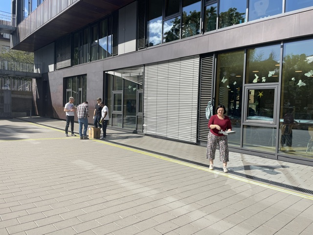 Eine Frau mit Unterlagen steht auf dem Schulhof der Mühlbergschule, im Hintergrund bereiten Helfer die Arbeiten beim Malteser Social Day vor