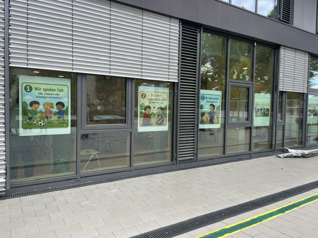 Neu angebrachte Schulregelplakate mit dem Titel „Wir spielen fair“ hinter der Fensterfront der Mühlbergschule
