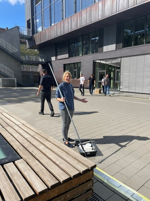 Eine Frau streicht mit einer Farbrolle auf langem Stiel Markierungen auf dem Schulhof der Mühlbergschule beim Malteser Social Day