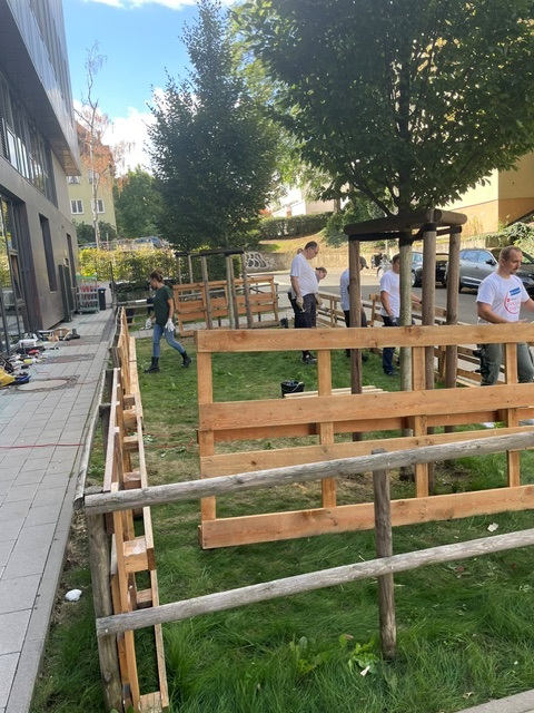 Aus Holzpaletten und Rundhölzern gebaute Umzäunung für das künftige Klassenzimmer im Freien auf der Wiese neben dem Schulhof der Mühlbergschule