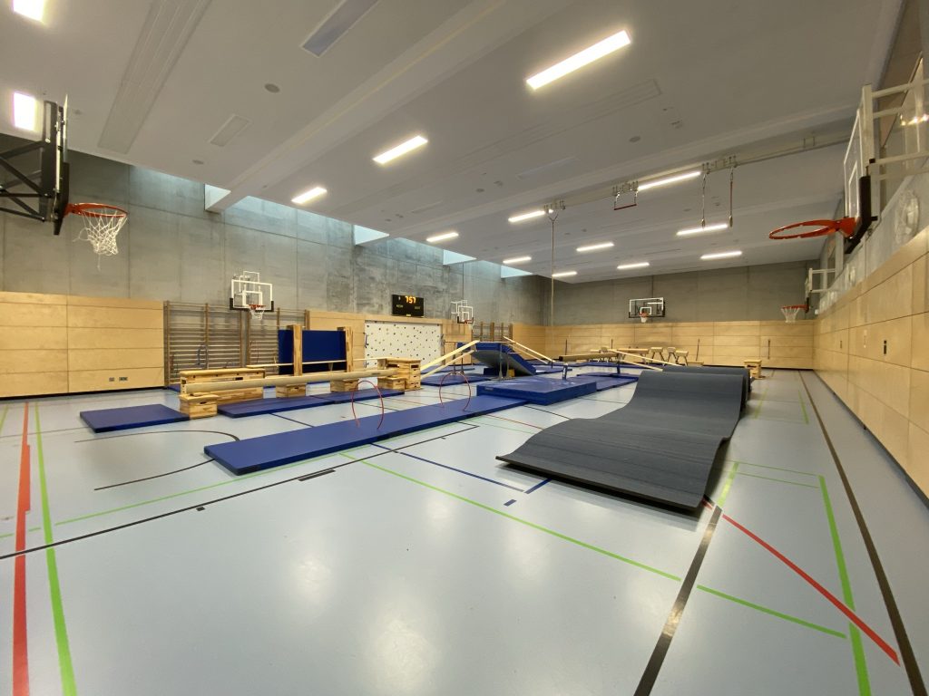 Weite Turnhalle mit Bänken, Matten und Gerätelandschaft für den Be Active Day Parcours