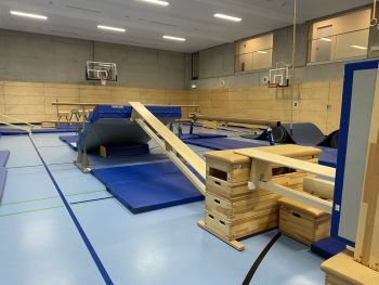 Schräge Bank über Kästen mit Matten und Weichboden in der Turnhalle, Be Active Day Parcours