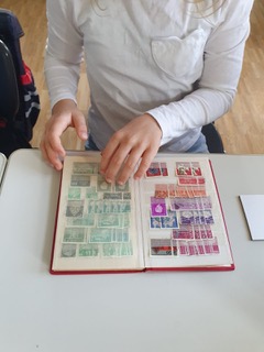 Kind blättert in einem Album mit Briefmarken, Briefmarken-Workshop der Klasse 2b