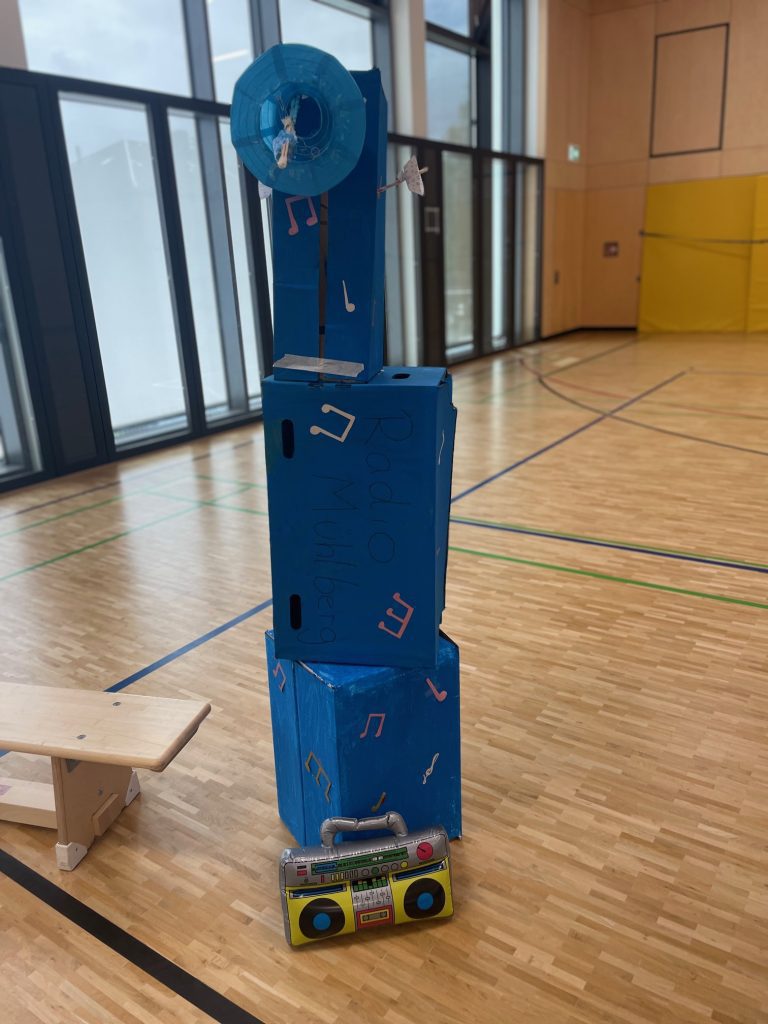 Blauer Turm aus Pappkartons mit Noten und Radio-Attrappe am Boden, Earsinnig hören Klasse 3e
