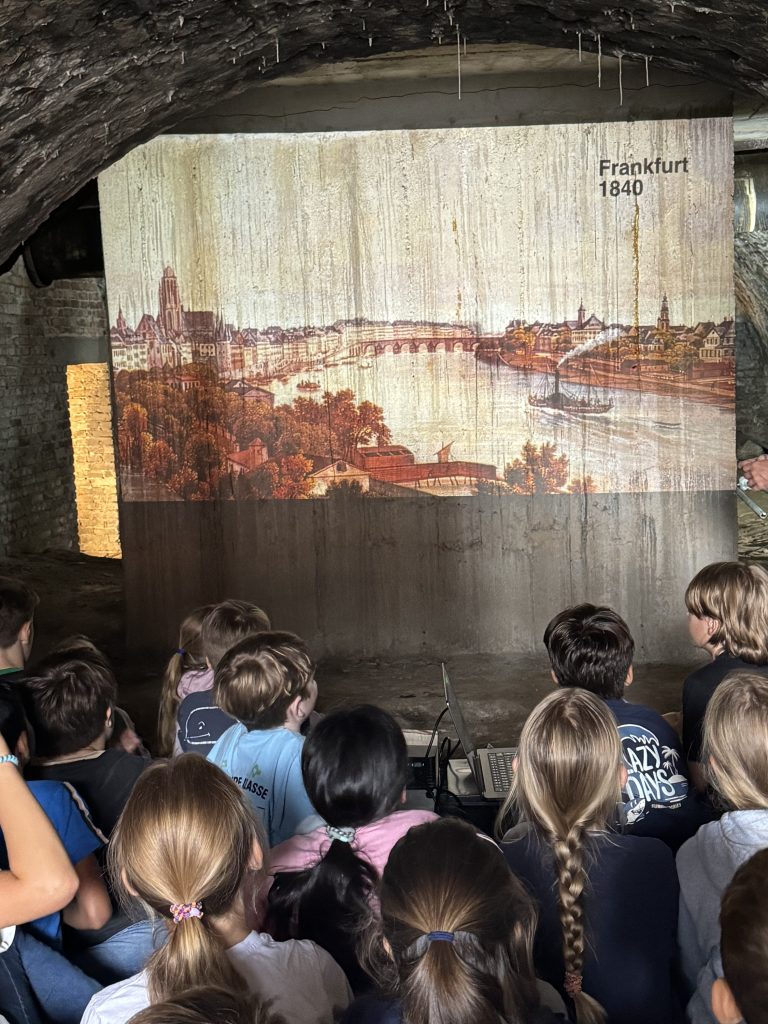 Kinder sitzen vor einer Wandprojektion mit historischer Ansicht von Frankfurt 1840, Fischerhallen-Führung