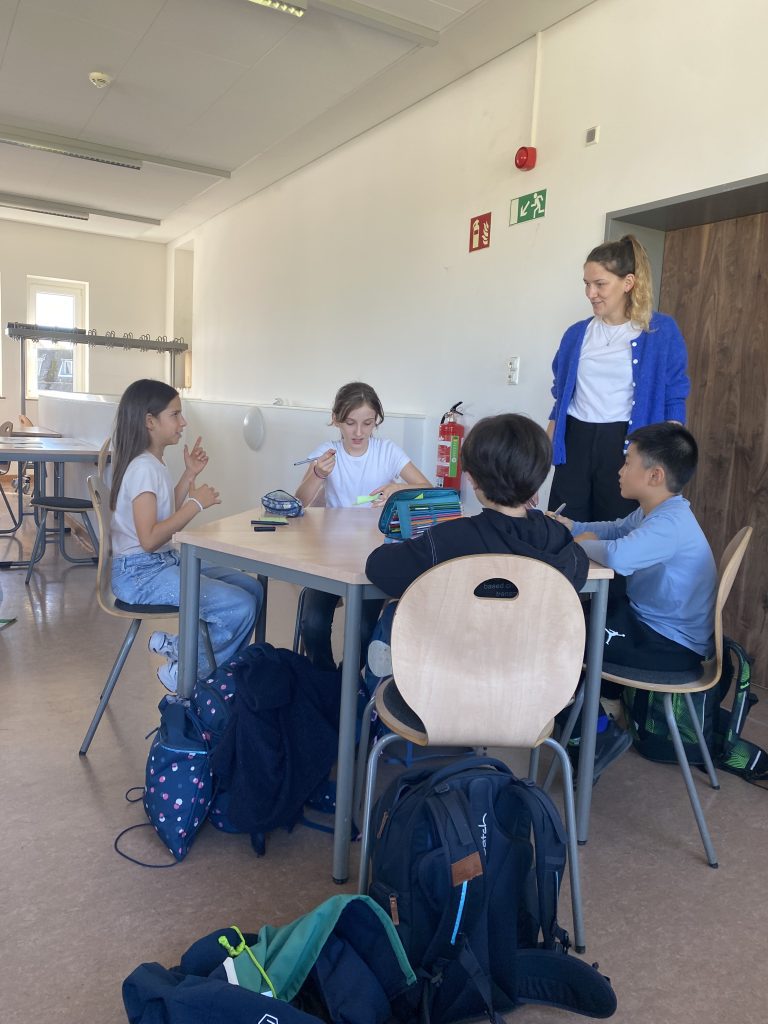 Kinder knobeln an einem Gruppentisch, eine Leiterin steht daneben, Mathematikworkshop der Schillerschule